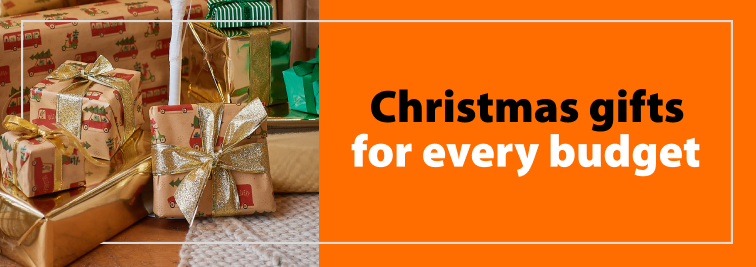 A customer and Mitre 10 staff member walk through a Mitre 10 store carrying wrapping paper and a trolley full of product. Accompanied by a heading "Loads of Christmas gift ideas to suit your budget"