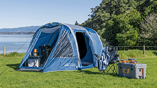 A large blue tent be the beach with a camping chair and chilly bin next to it