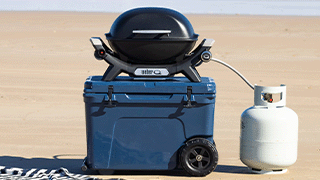 A Weber BBQ sitting on a chilly bin on the beach